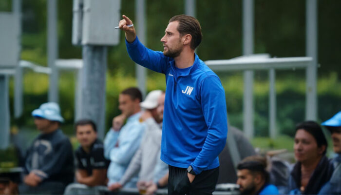 Hoofdtrainer Joren van V.V. Albatross coacht fanatiek vanaf de zijlijn tijdens een wedstrijd, gekleed in een blauw trainingsjack met initialen 'JW'.