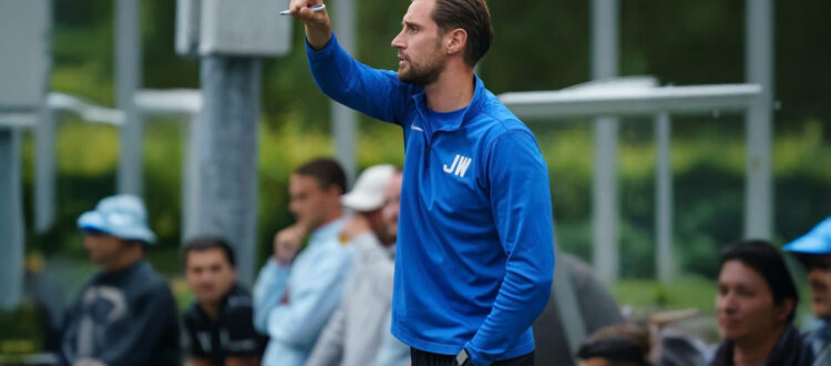 Hoofdtrainer Joren van V.V. Albatross coacht fanatiek vanaf de zijlijn tijdens een wedstrijd, gekleed in een blauw trainingsjack met initialen 'JW'.